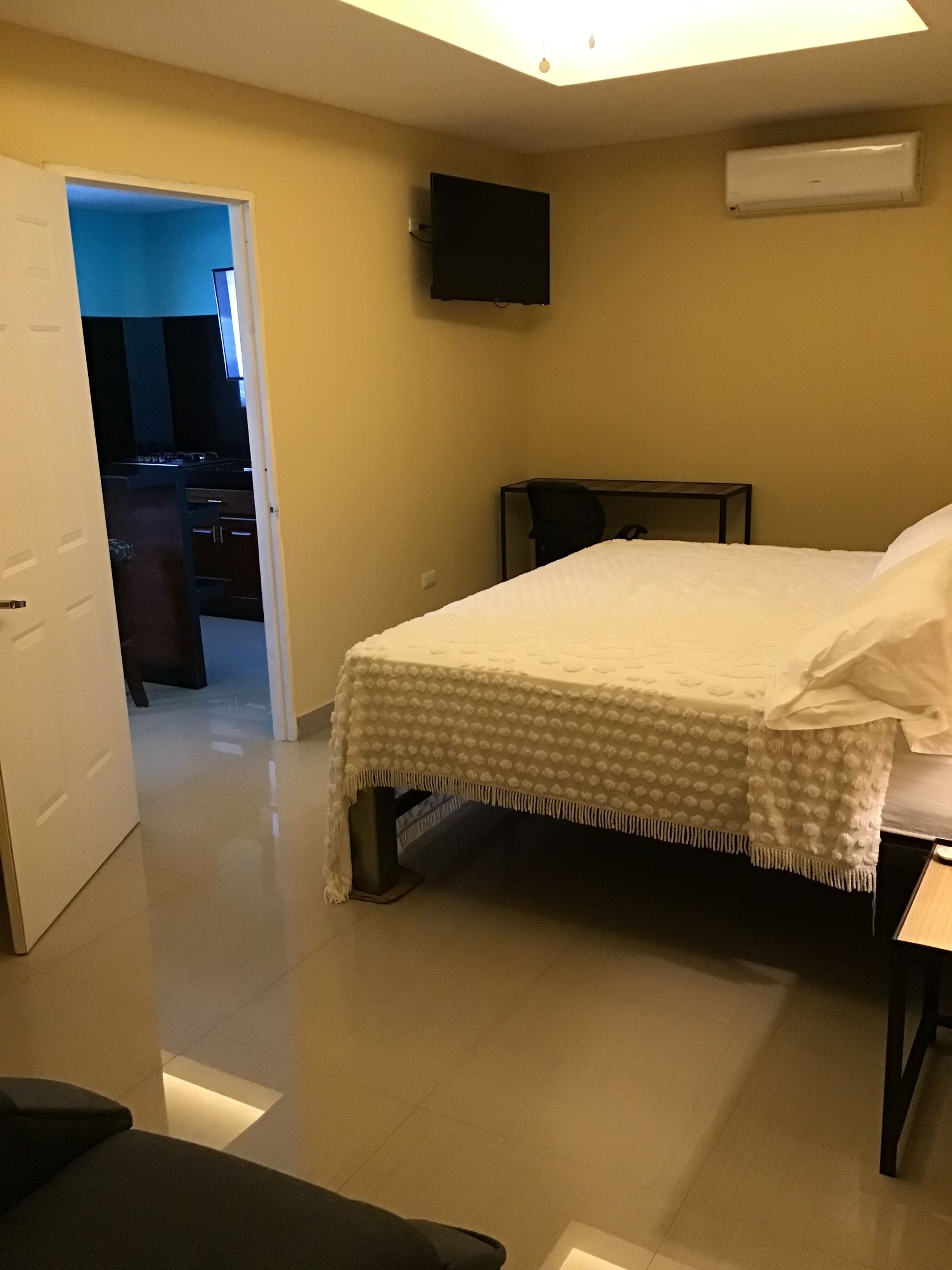 A hotel room with a bed, a TV mounted on the wall, and an air conditioning unit.