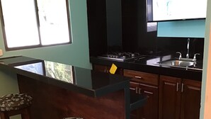 Eine Küche mit schwarzer Arbeitsplatte, Holzschränken und einer Bar mit zwei Hockern.