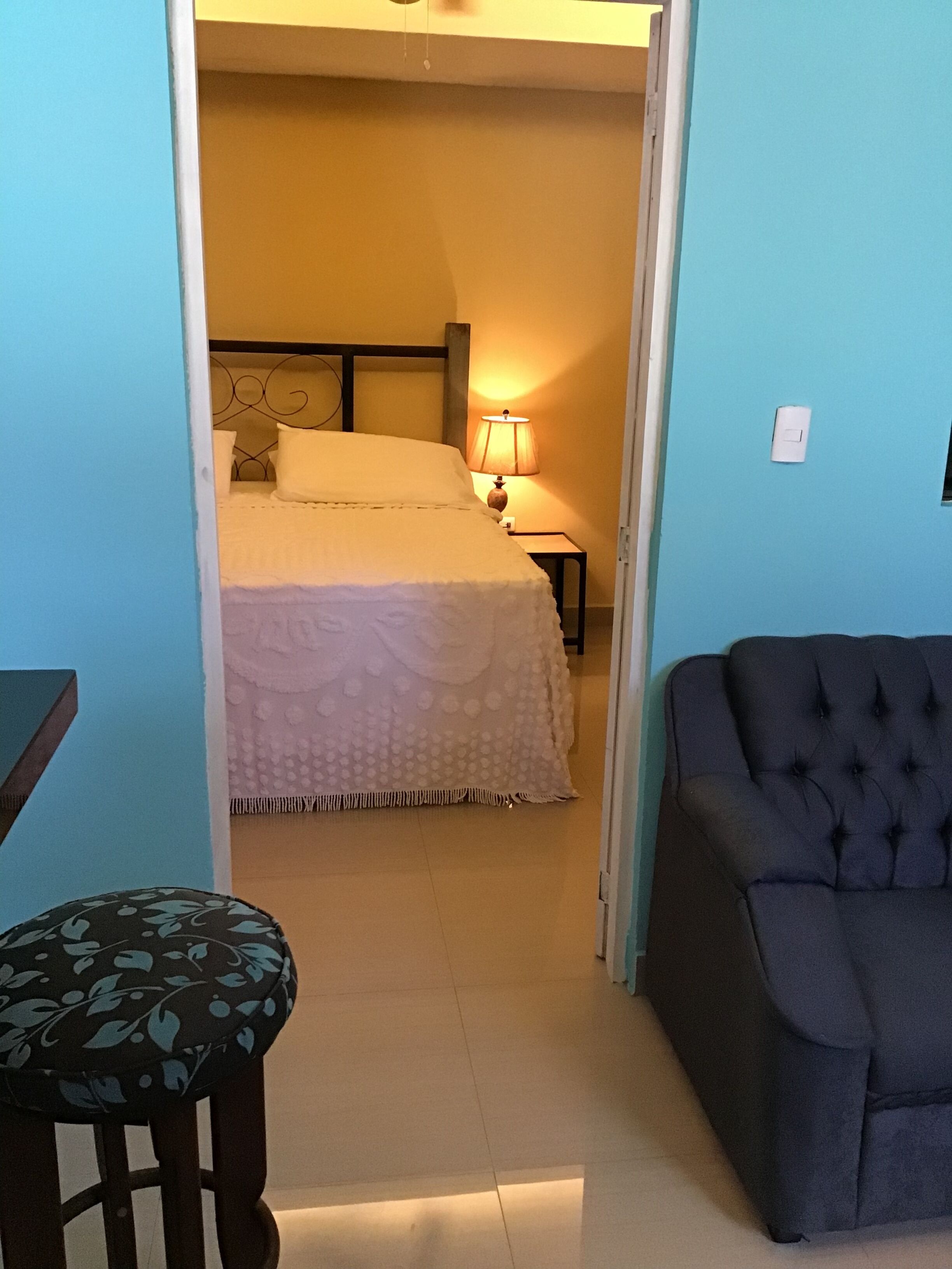 Una habitación con una cama, una mesita de noche con una lámpara, una silla y un taburete pequeño.