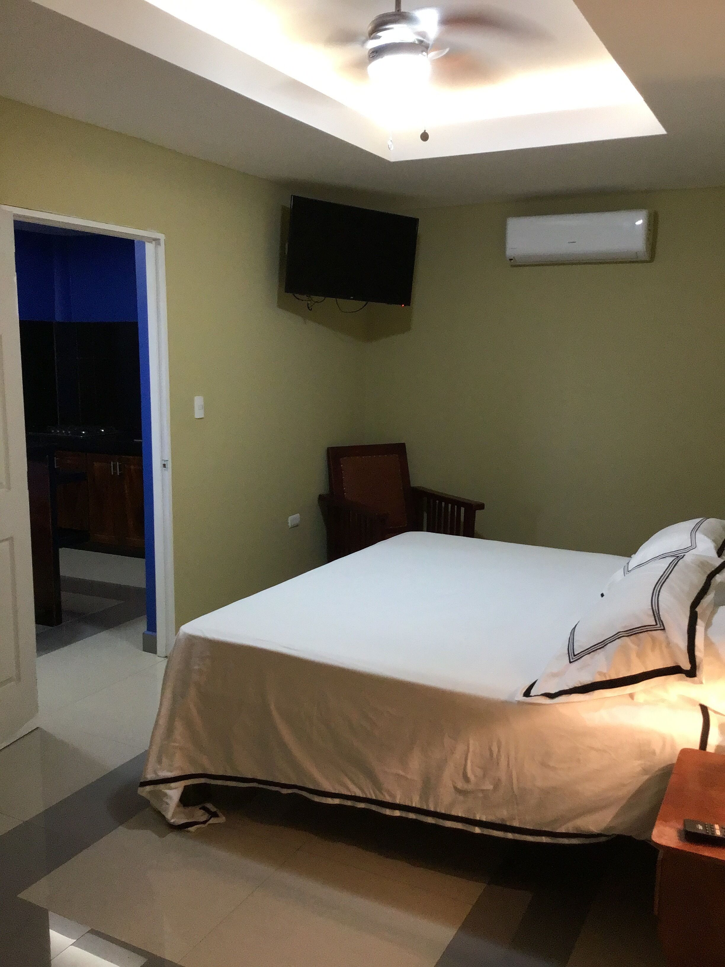 A bedroom with a bed, a television mounted on the wall, and a ceiling fan.