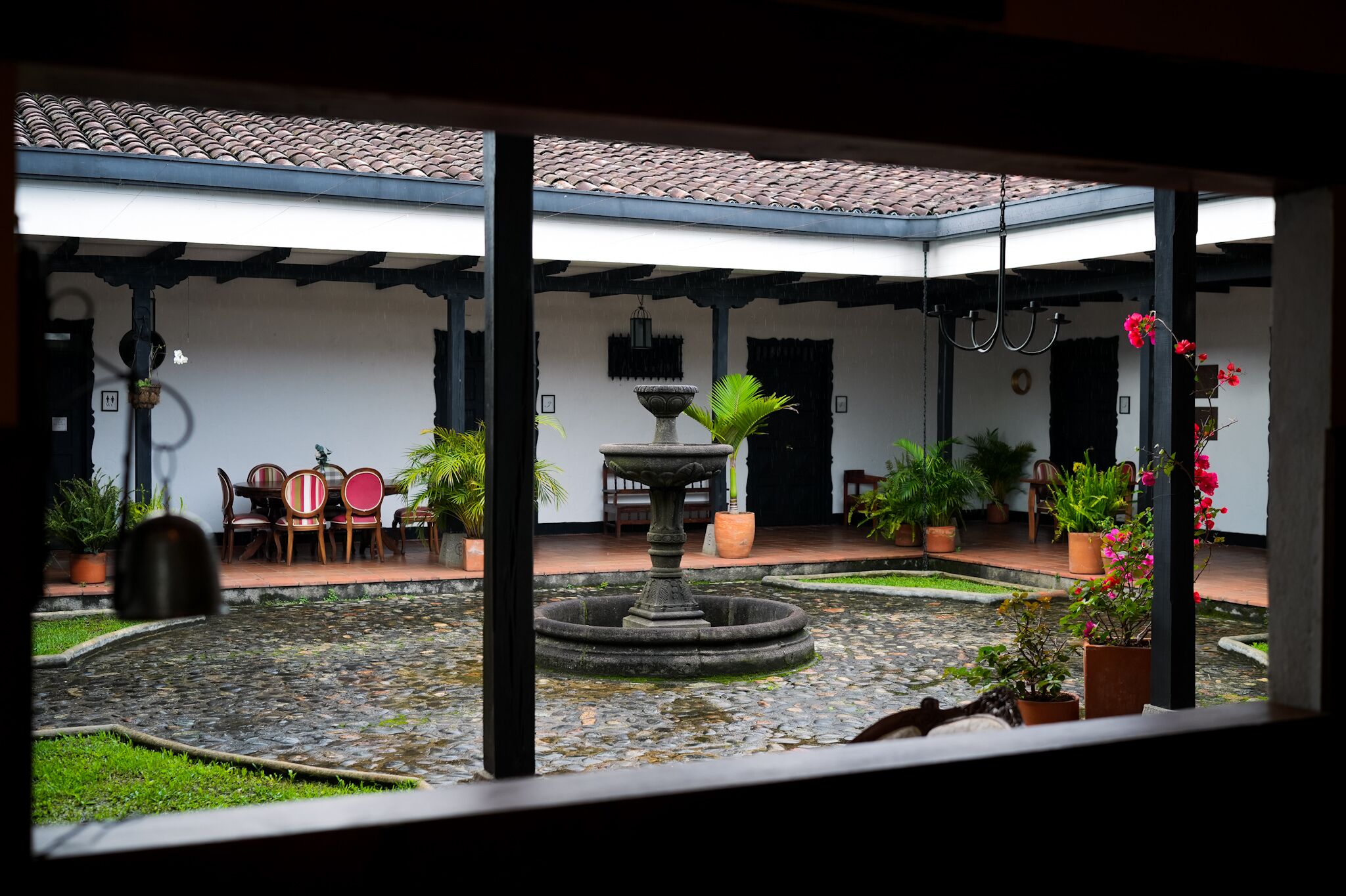 Un patio con una fuente, plantas en macetas y mesas al aire libre.