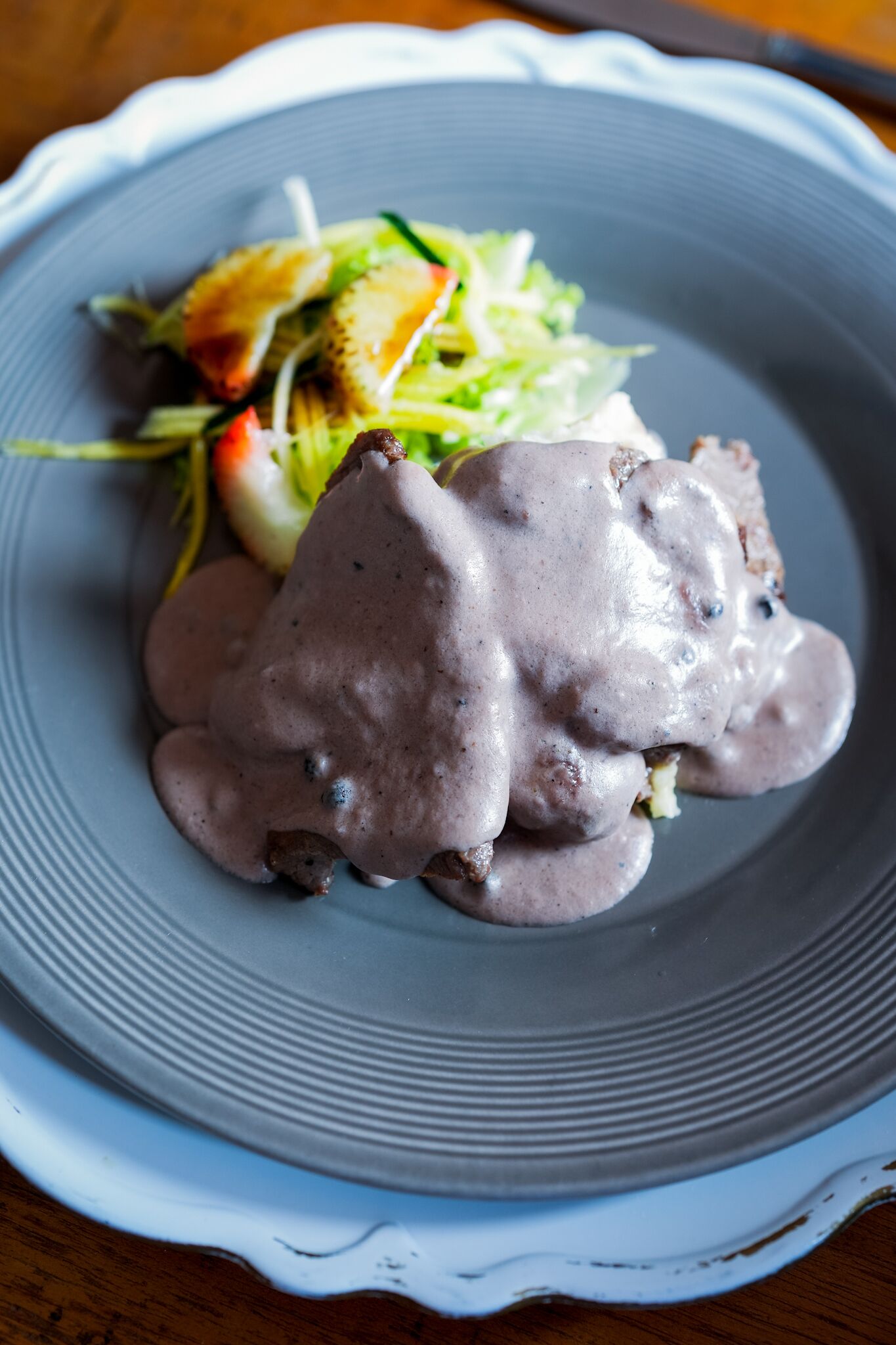 A plate with a food item covered in a creamy sauce, accompanied by a side salad.