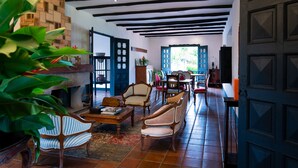 A spacious living room with a fireplace, multiple chairs, a coffee table, and a view of the outdoors through a large window. - Hotel Hacienda Supracafe (Cajibío)