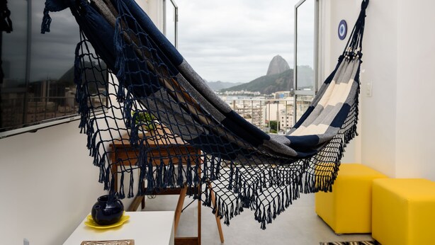 A hammock chair in a room with a view of a cityscape and a mountain.