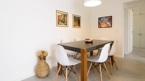 A dining area with a wooden table, white chairs, and framed artwork on the wall.