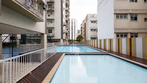 A swimming pool with a wooden deck and white railings, surrounded by multi-story residential buildings.