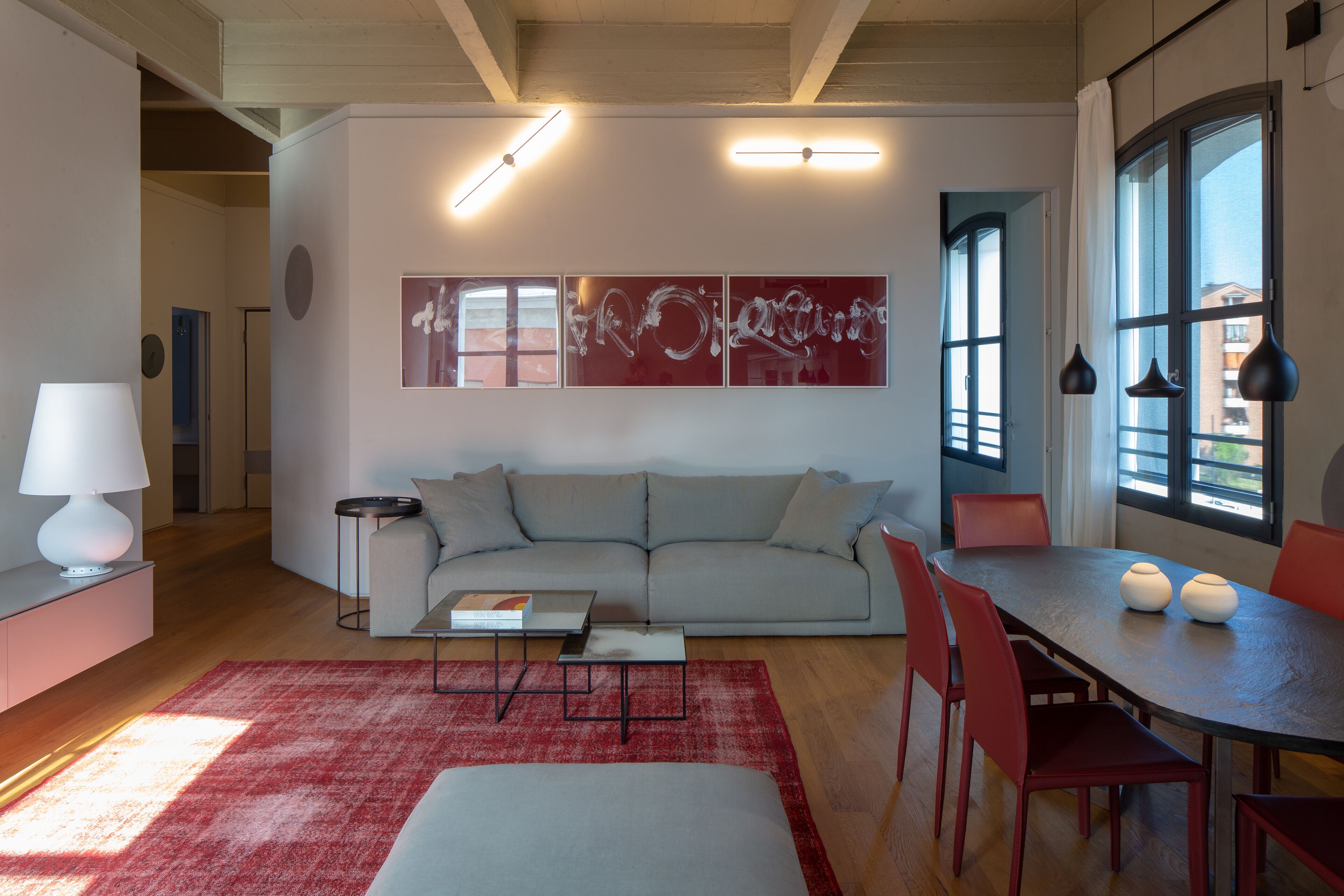 A modern living room with a grey sofa, red chairs, a dining table, and a red rug.
