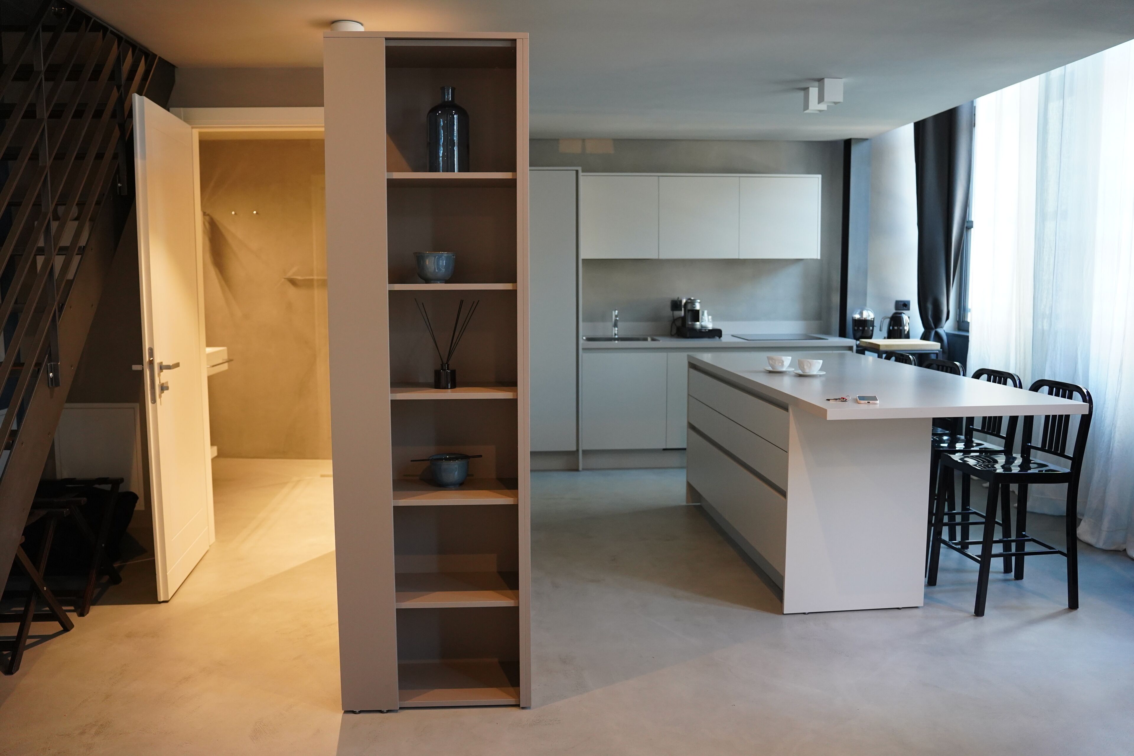 Una cocina moderna con una isla central, armarios blancos y una escalera a la izquierda.