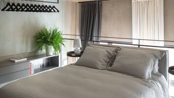 Un dormitorio moderno con una cama grande, mesitas de noche, una planta en maceta y vistas de la ciudad a través de amplios ventanales.