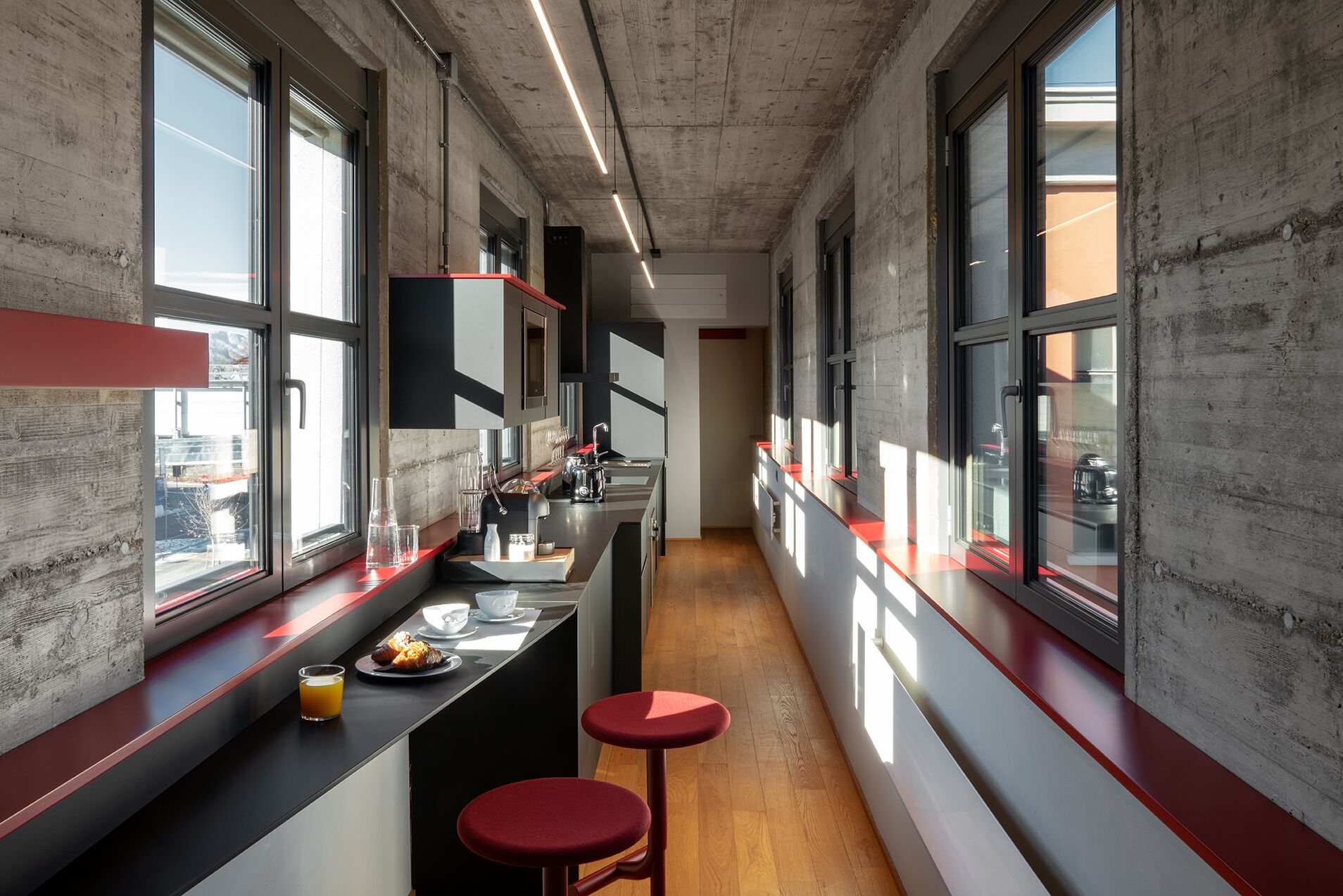 A narrow, industrial-style kitchen with large windows and a long countertop.