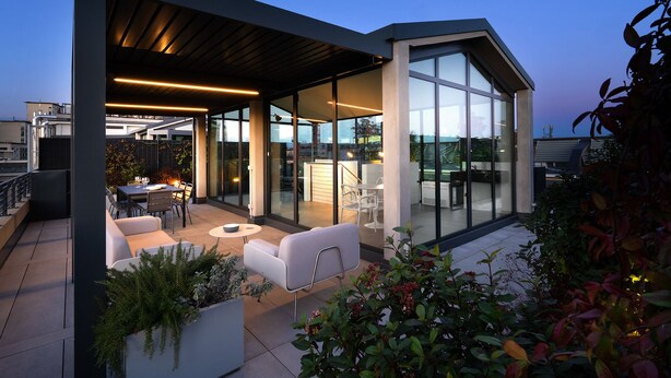 A modern rooftop patio with a glass enclosure, outdoor furniture, and a view of the cityscape. - Edit Lofts  (Turin)