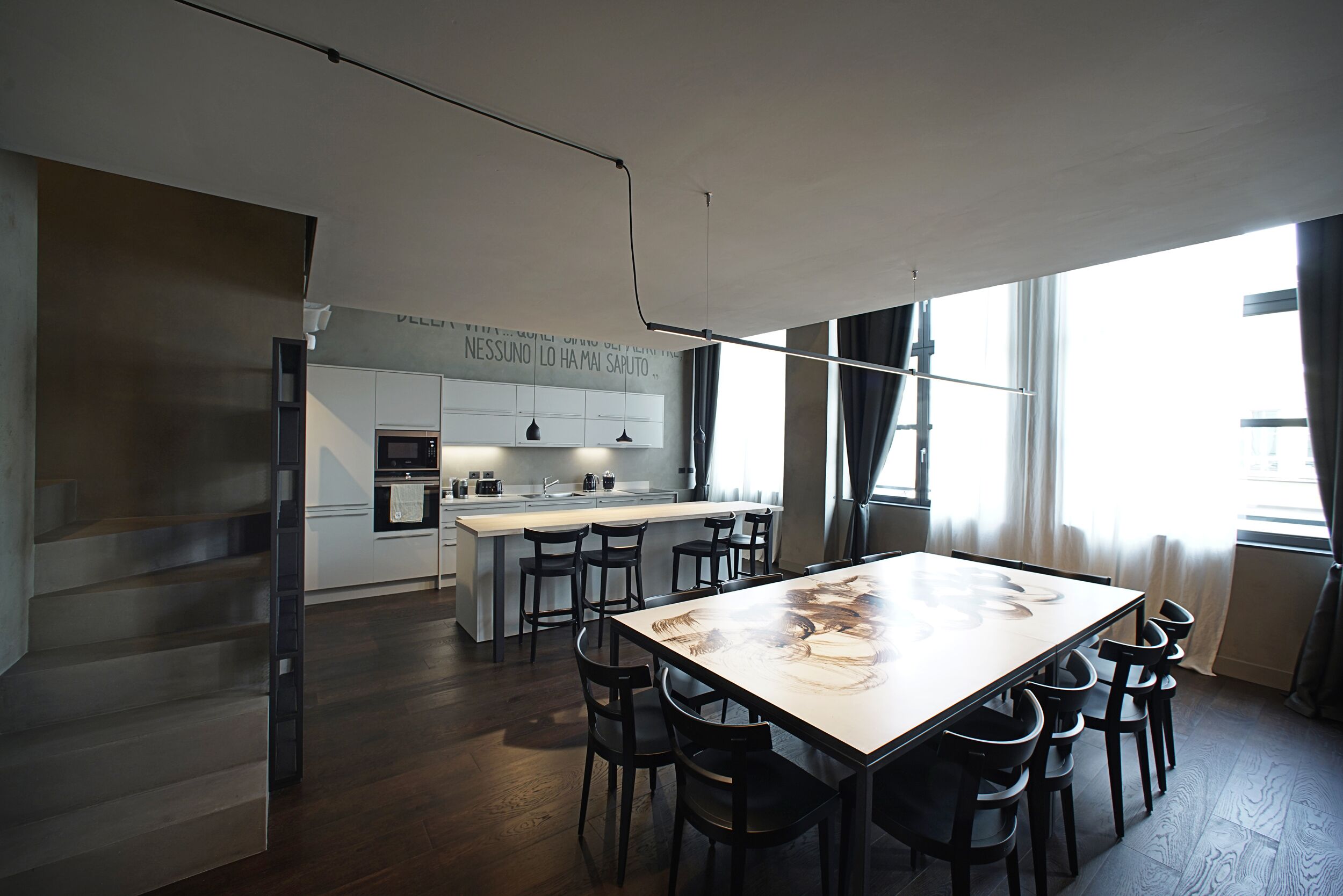 A modern kitchen with a central island, a dining area with a large table and chairs, and a staircase leading to an upper level.