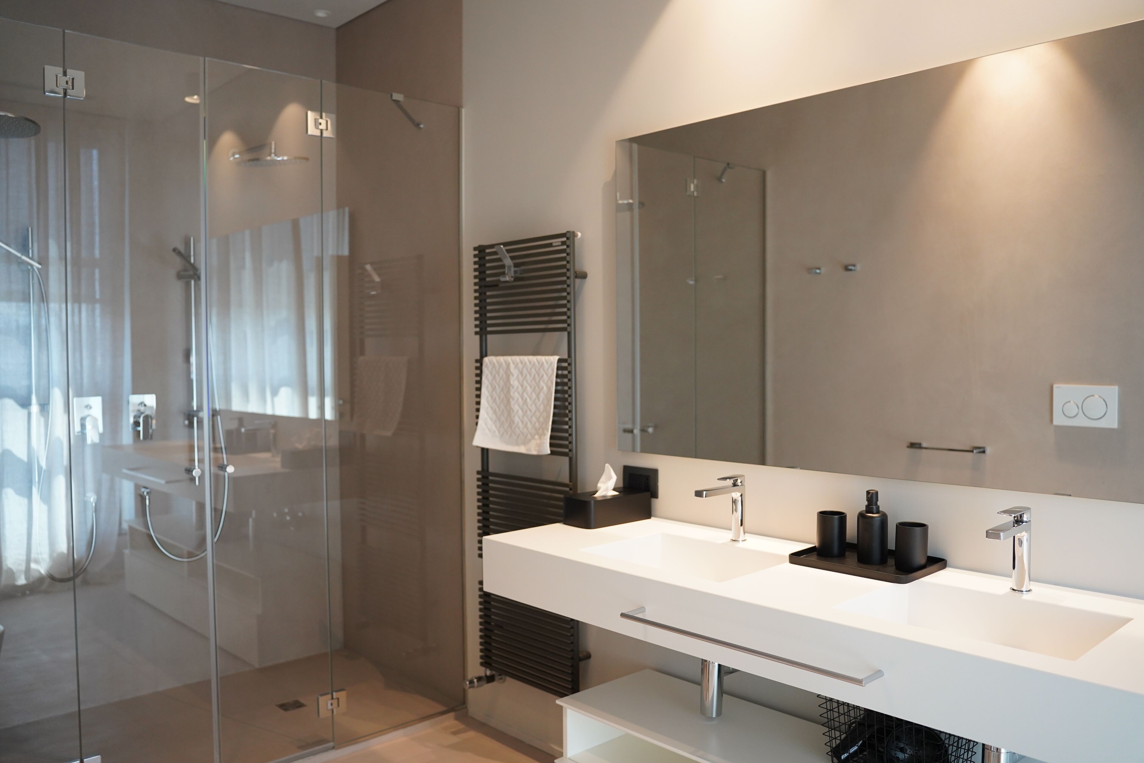 Un baño moderno con cabina de ducha de vidrio, un espejo grande y un mueble de tocador blanco con dos lavamanos.