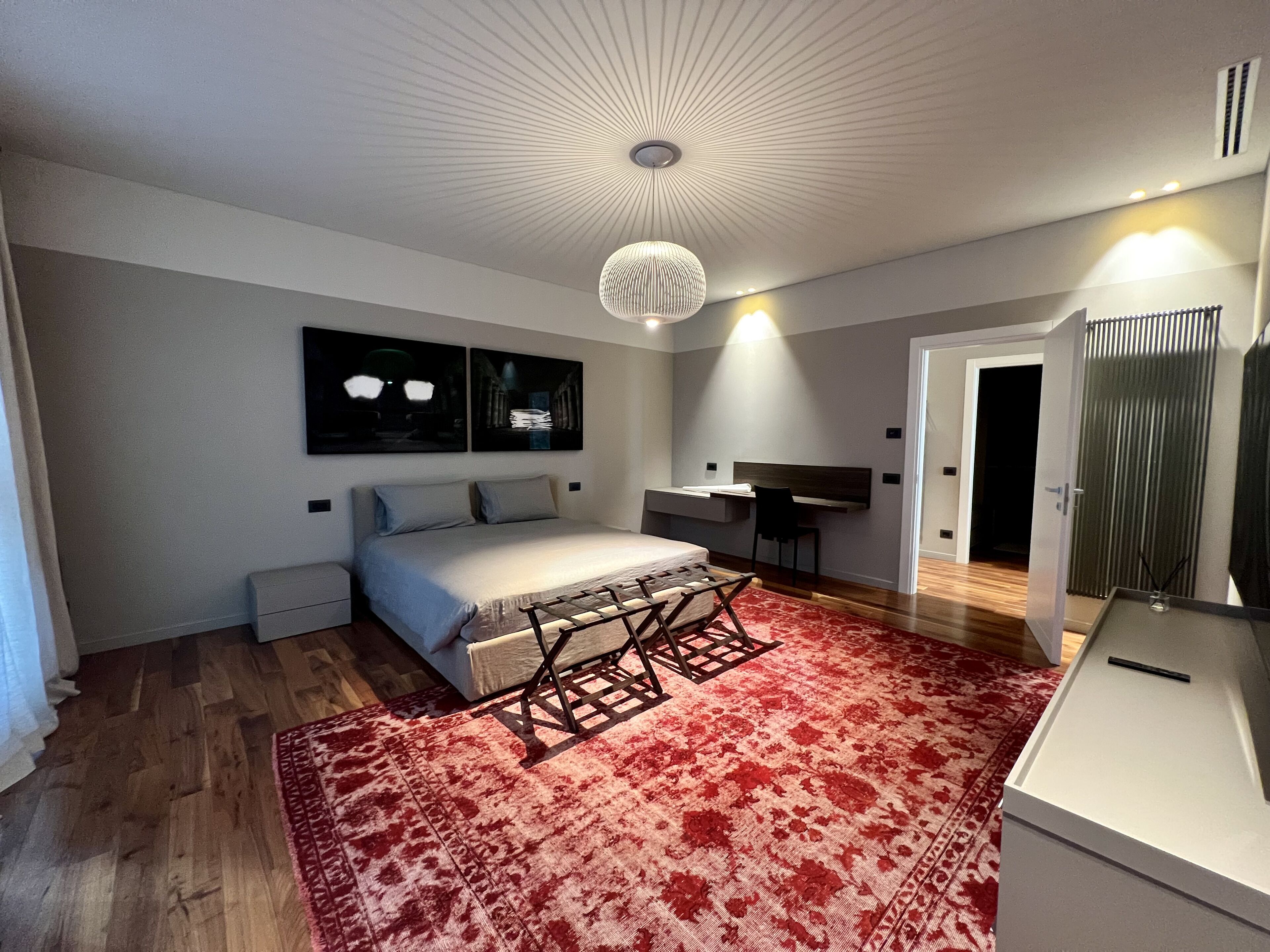 A modern bedroom with a bed, a desk, and a red patterned rug.