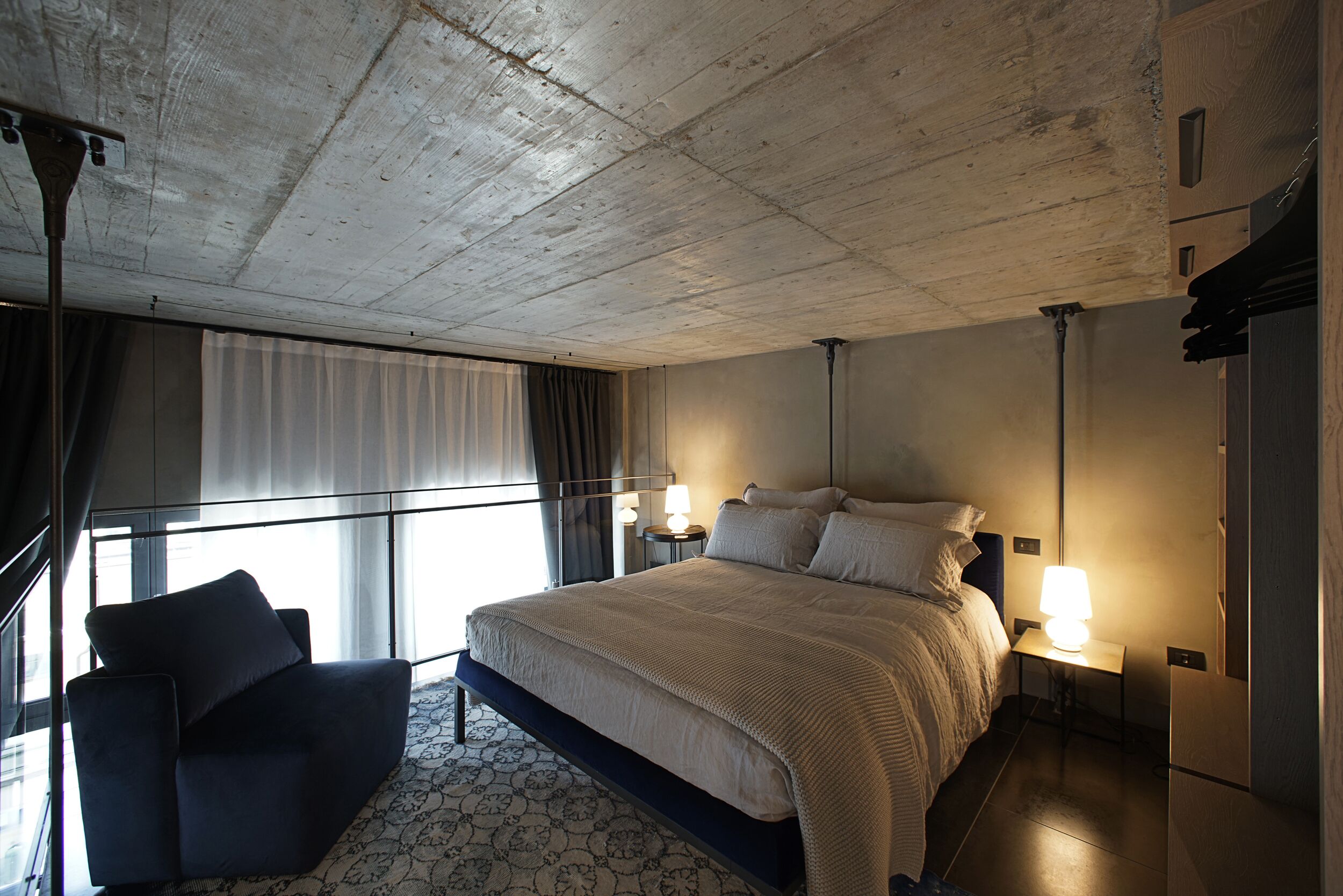 Camera d'albergo con un letto grande, un divano, un comodino con una lampada e vista all'esterno attraverso una finestra con tende.