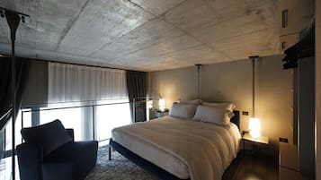 Camera d'albergo con un letto grande, un divano, un comodino con una lampada e vista all'esterno attraverso una finestra con tende.