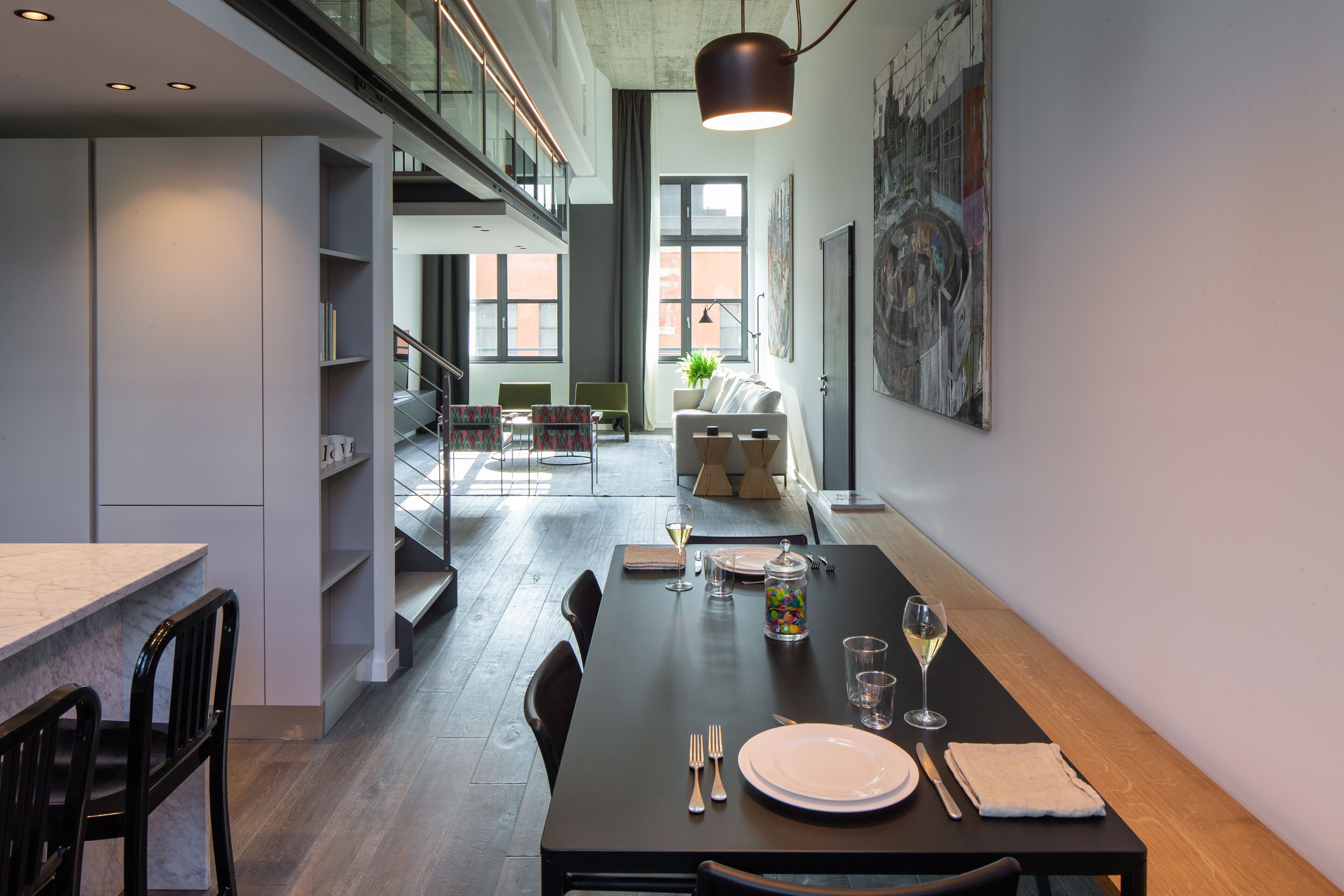 Un comedor moderno con una larga mesa dispuesta para dos, una escalera y vistas de la ciudad a través de amplios ventanales.