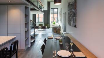 Un comedor moderno con una larga mesa dispuesta para dos, una escalera y vistas de la ciudad a través de amplios ventanales.