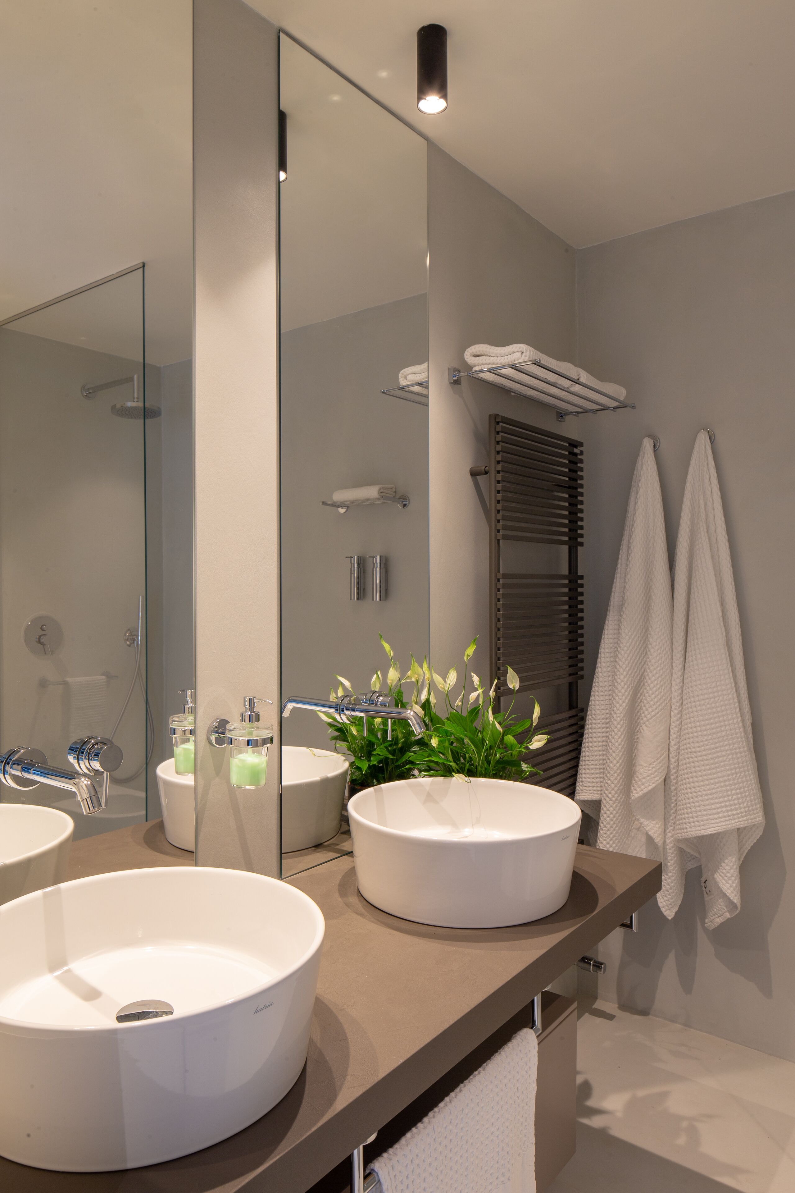 Un baño moderno con dos lavamanos redondos blancos, un espejo grande y un perchero para toallas.