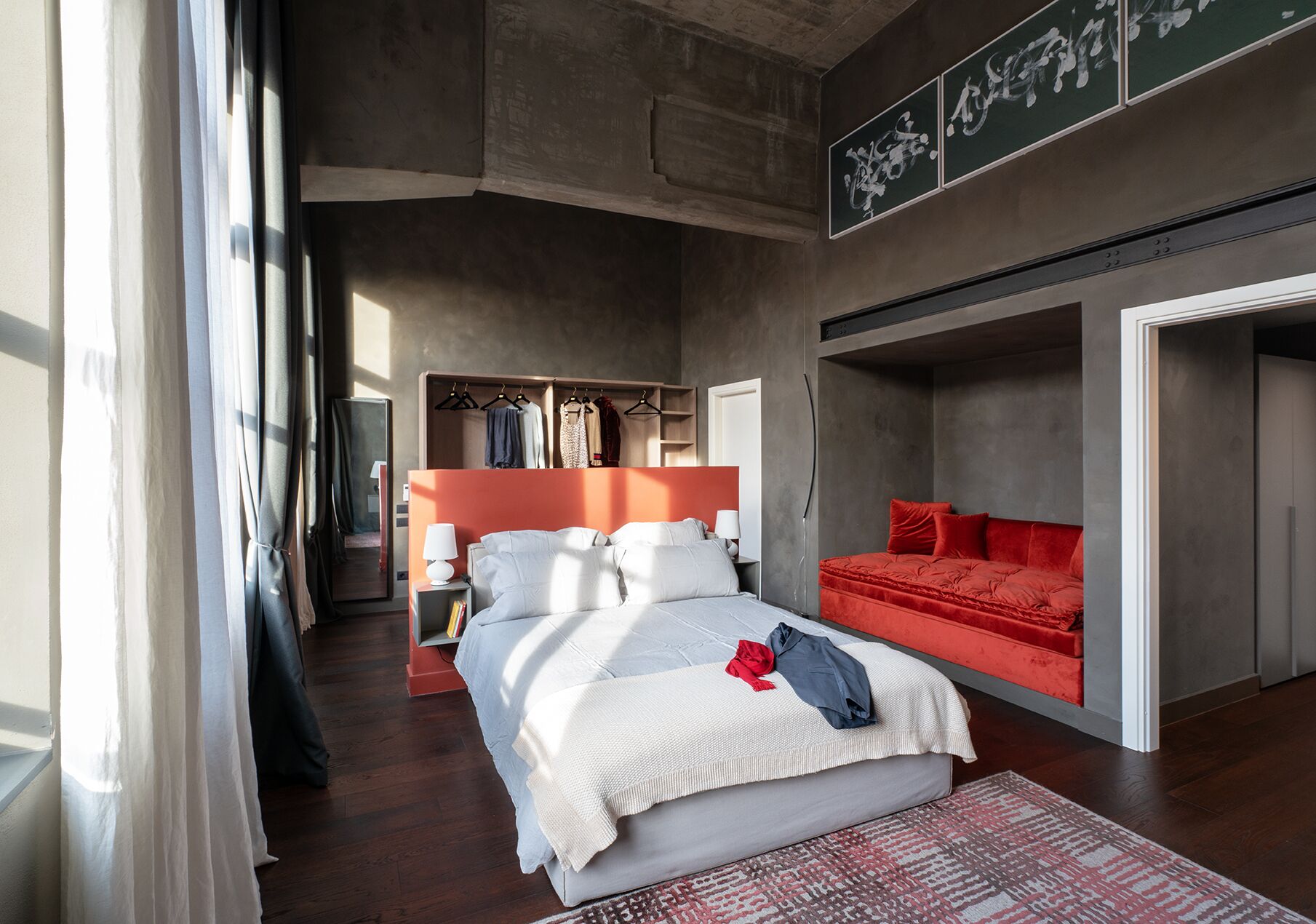 A modern bedroom with a large bed, a red sofa, and a walk-in closet.