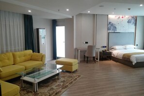 A modern hotel room with a yellow sofa, a glass coffee table, a bed, a desk, and a large artwork on the wall. - Crowne International Business Hotel (Shiyan)