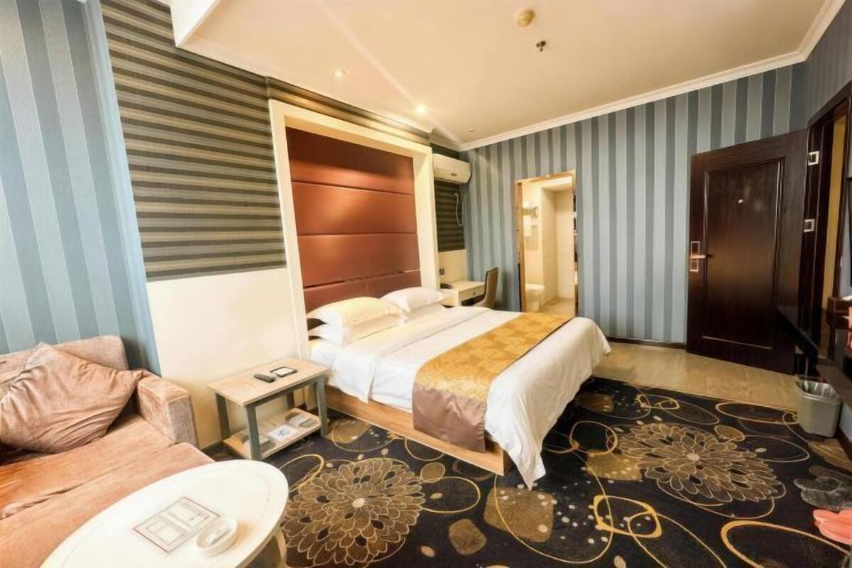 Una habitación de hotel con una cama, mesita de noche, lámpara y un sofá.