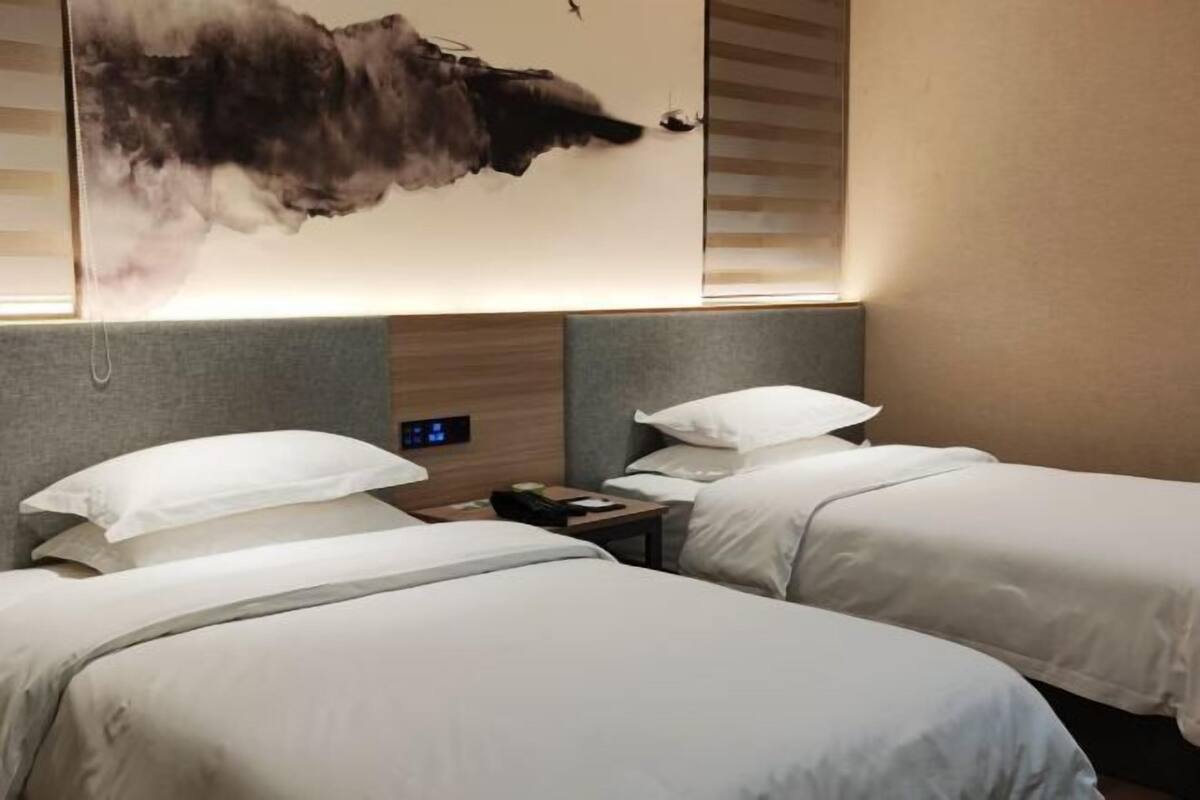Una habitación de hotel con dos camas, un reloj fijado a la pared y un cuadro abstracto grande.