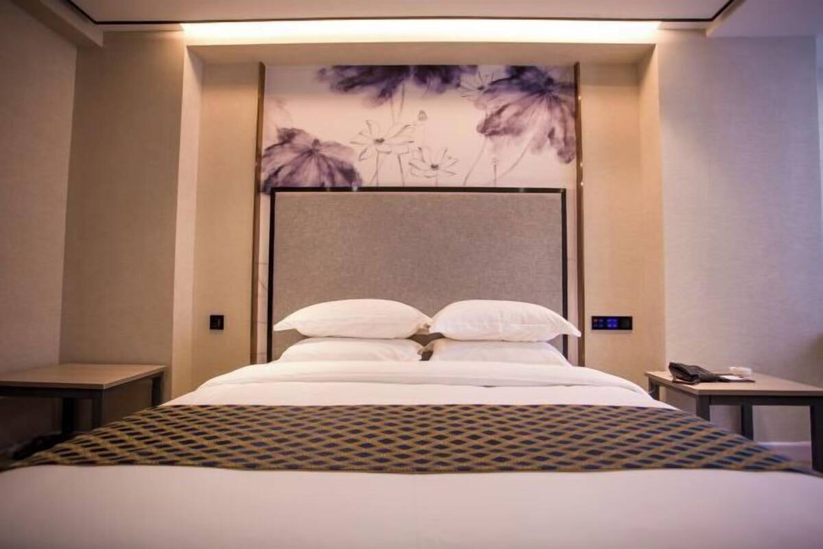 Una habitación de hotel con cama, mesita de noche, teléfono en la pared y un panel decorativo con motivos florales.