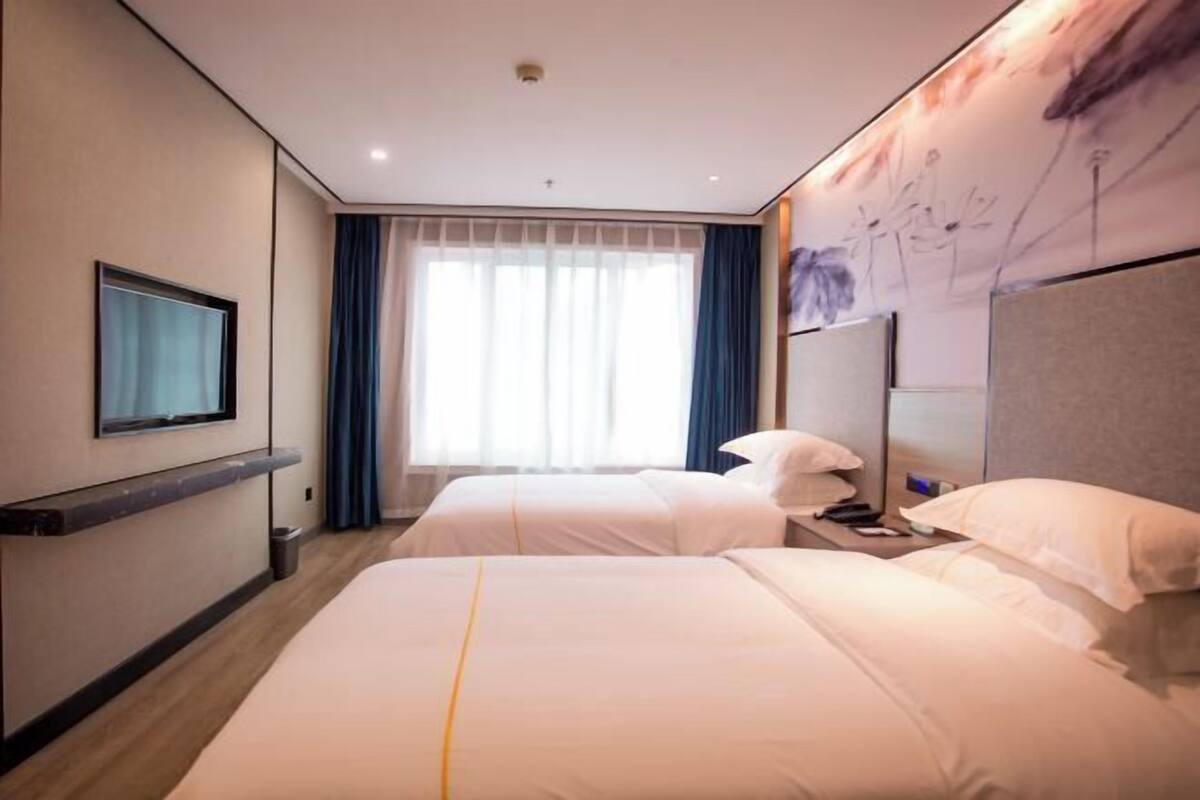 Habitación de hotel con dos camas, televisión, un ventanal grande con cortinas y una obra de arte colgada en la pared.