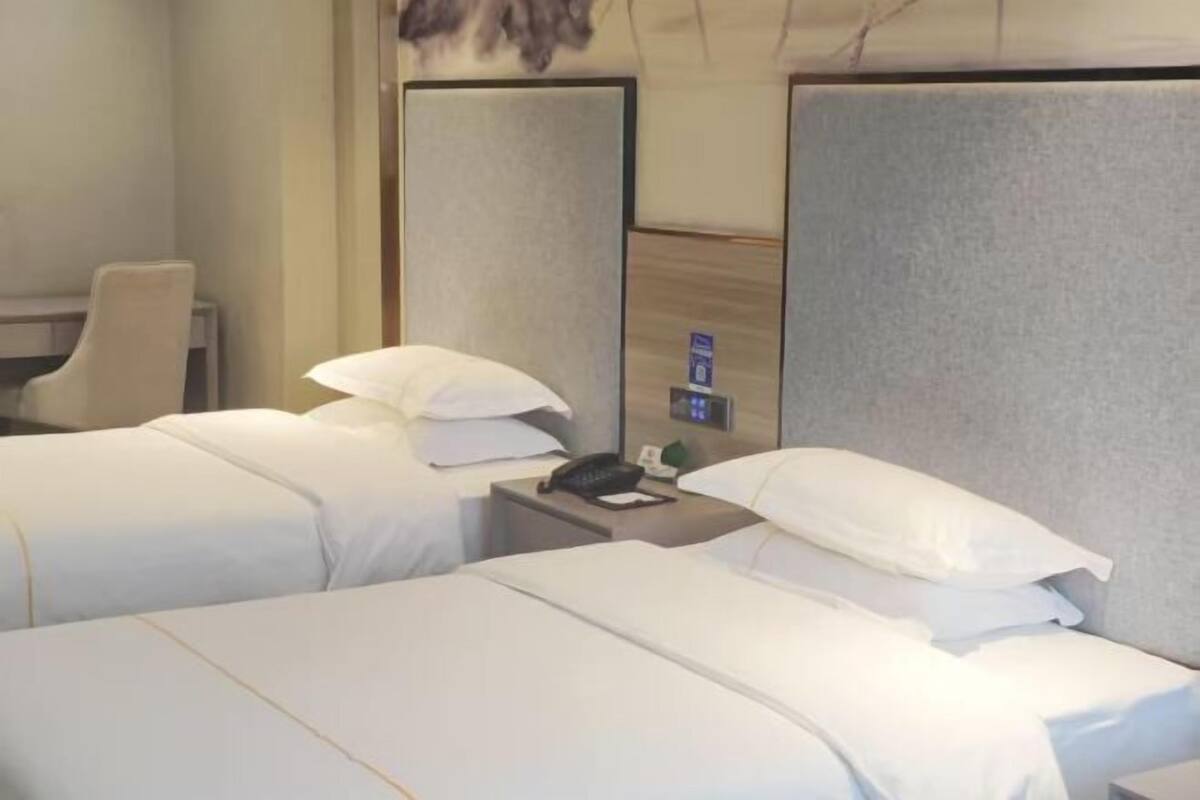 Habitación de hotel con dos camas, un escritorio, una silla, una mesita de noche con un teléfono y un panel de control en la pared.