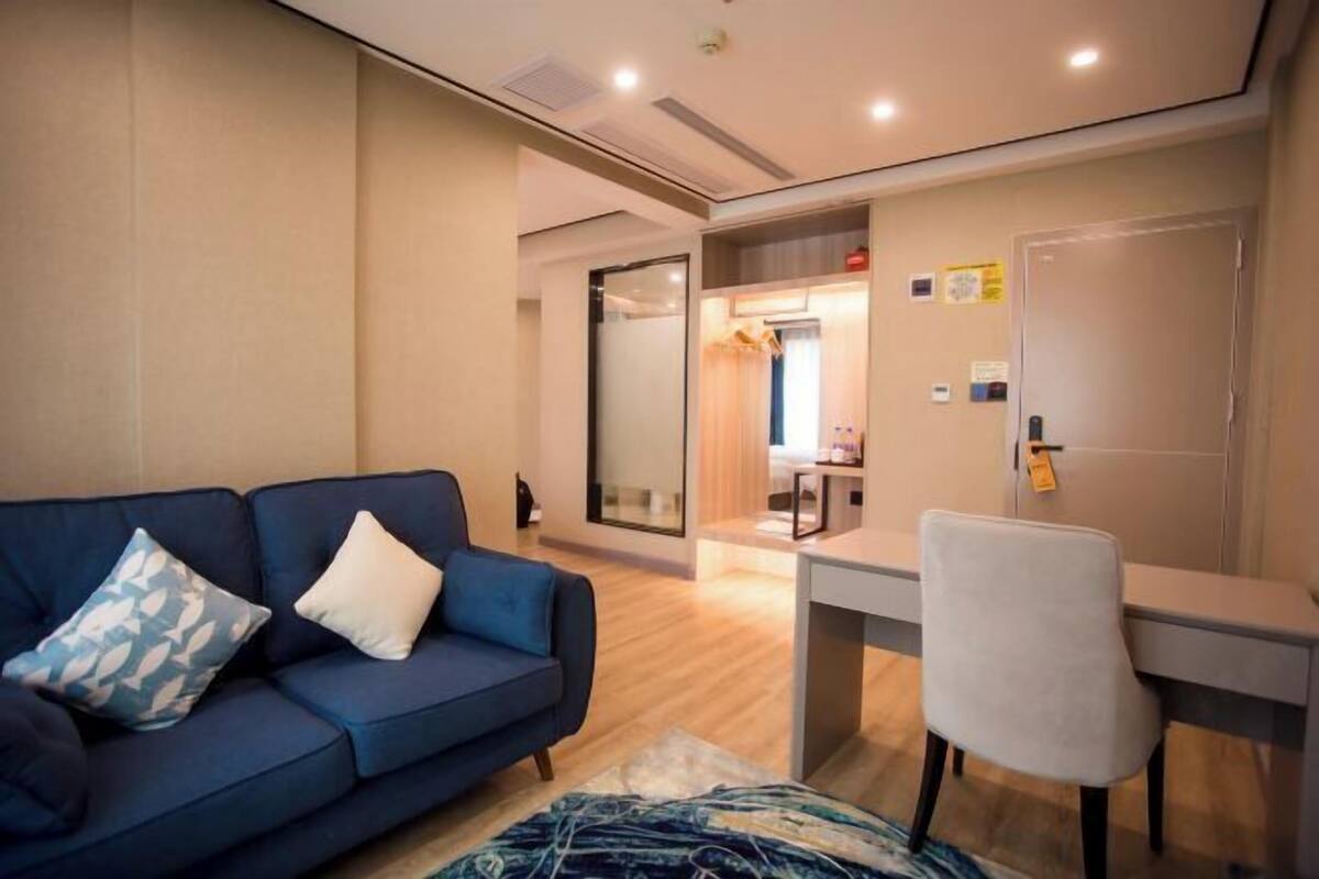 Una habitación moderna con un sofá azul, una silla blanca, un escritorio y una puerta de vidrio que da al baño.