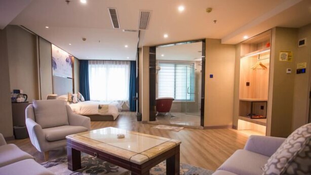 A hotel room with a bed, a sitting area with a coffee table, a sofa, and a wardrobe. - Crowne International Business Hotel (Shiyan)