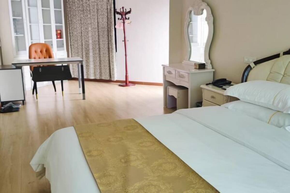 Habitación de hotel con cama, escritorio, silla, perchero, cómoda y espejo.
