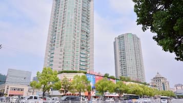 Un edificio alto con varios pisos, rodeado de árboles y una calle con vehículos.