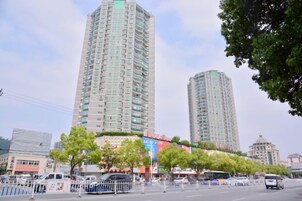 Un edificio alto con varios pisos, rodeado de árboles y una calle con vehículos.