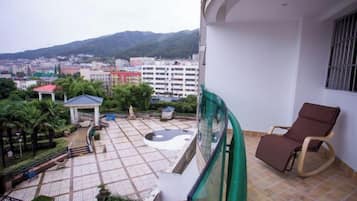 A balcony with a view of a cityscape, a chair, and a small garden area.
