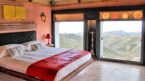 A large bed with a red blanket, a bedside table with a red lamp, and a view of mountains through a large window. - Villa Musolino Country Resort (Messina)