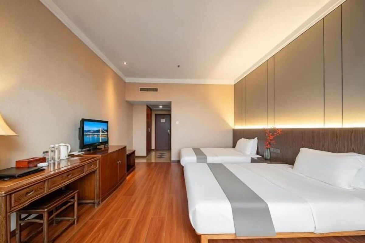 Camera d'albergo con una scrivania in legno, una televisione, due letti e vista sulla città.