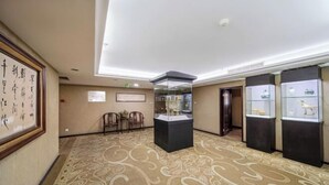 Un hall de hotel con alfombra estampada, una vitrina de cristal y caligrafía enmarcadas en la pared.