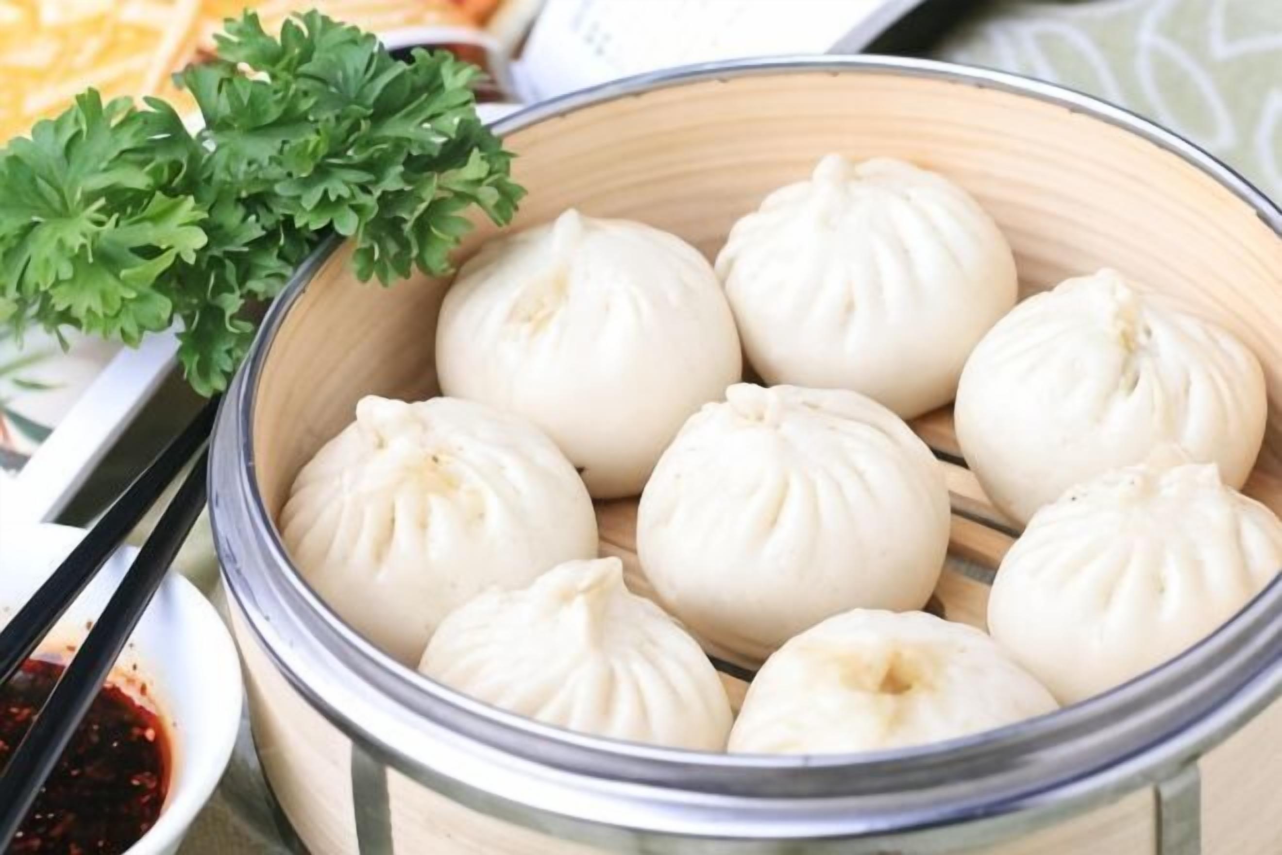 A steamer basket with white steamed buns and a small bowl of red dipping sauce.