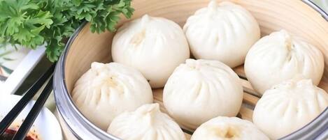 A steamer basket with white steamed buns and a small bowl of red dipping sauce.