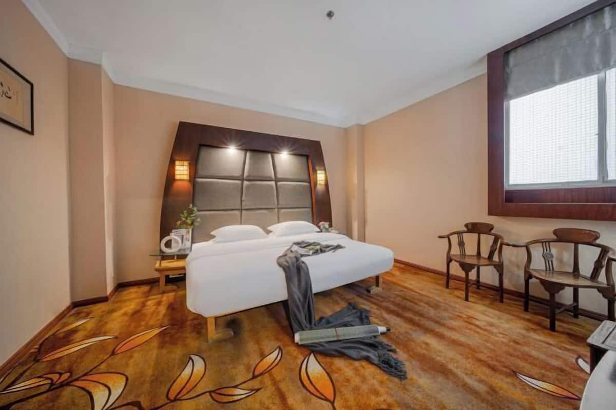 A hotel room with a large bed, a nightstand, a chair, and a window.