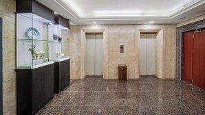 Vestíbulo con suelo de mármol, vitrinas de cristal y dos ascensores.