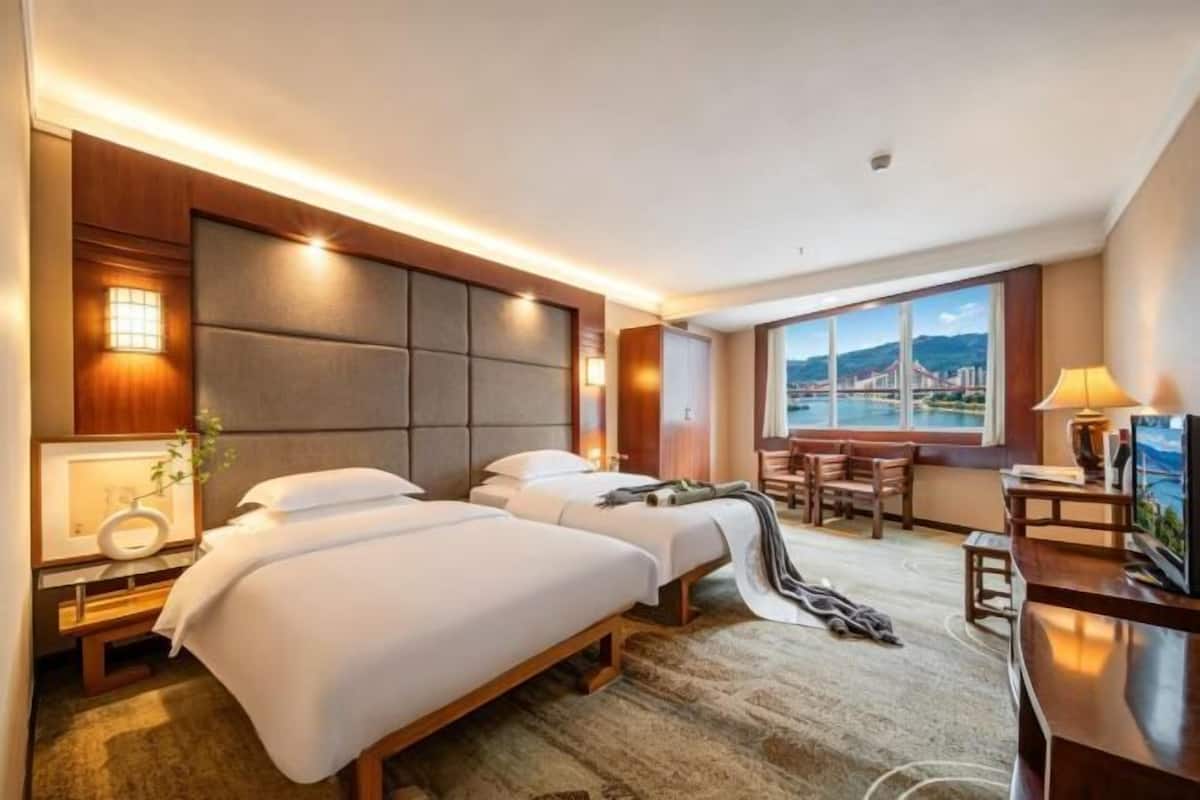 A hotel room with two beds, a desk, a TV, and a large window with a view.