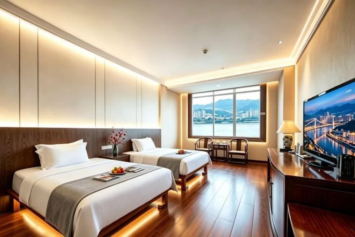 A hotel room with two beds, a TV, a desk, and a view of a cityscape.