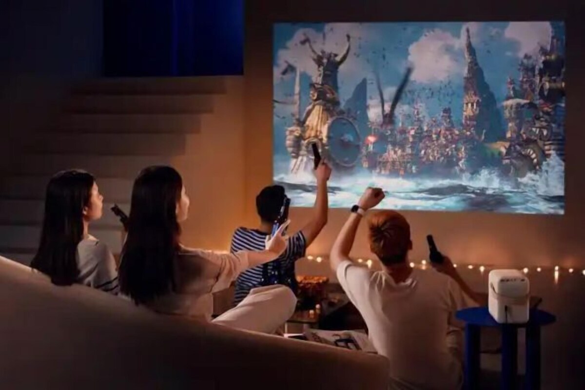A group of people watching a movie on a large screen in a cozy room with a staircase and string lights.