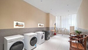 Un cuarto de lavado con varias lavadoras, un tendedero y una zona de estar con sillas.