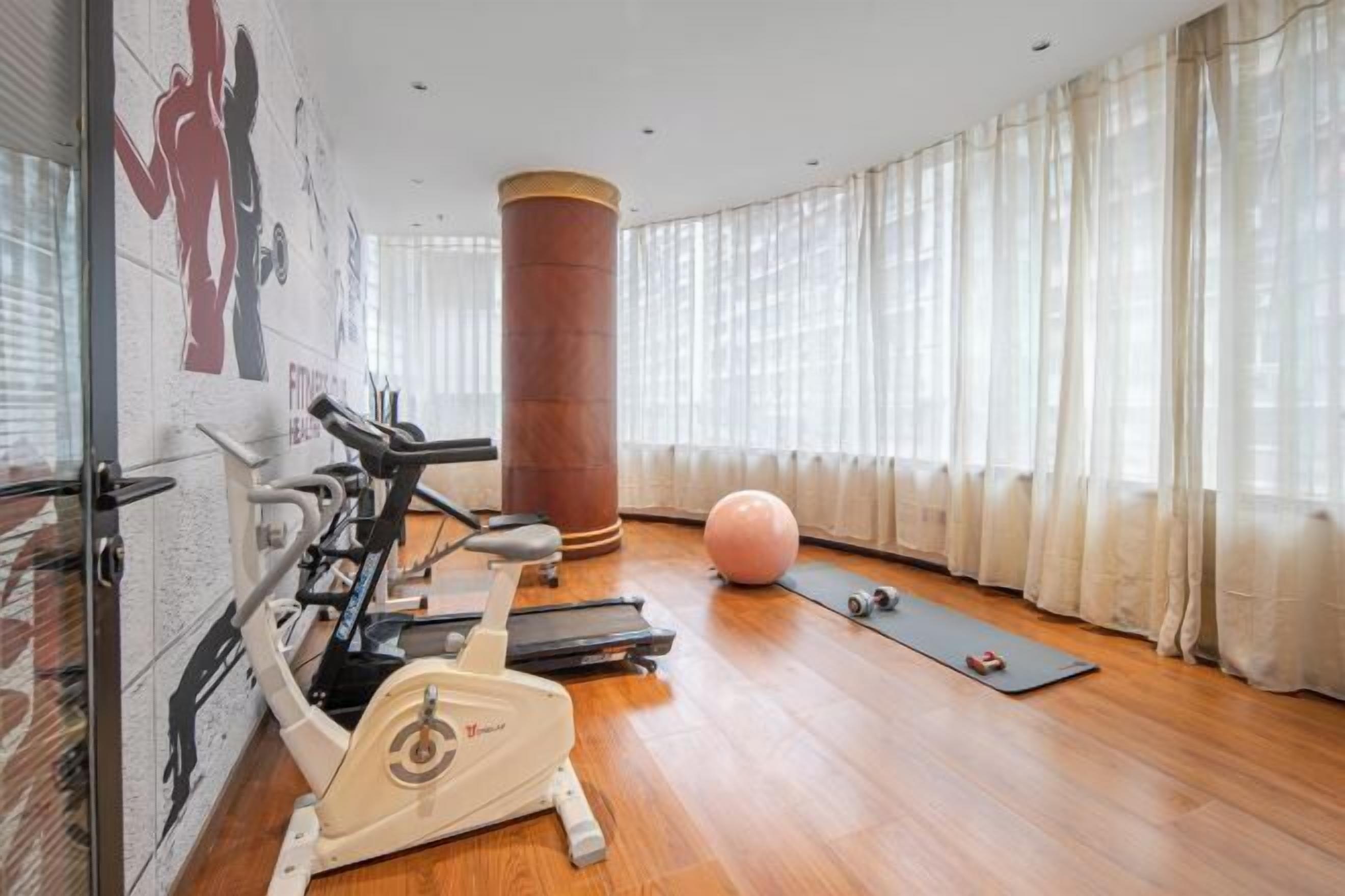 A gym with exercise equipment, a large pillar, and a yoga mat.