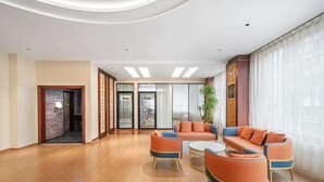 Un amplio vestíbulo con piso de madera, sofás naranja y azul, una mesa de centro redonda y un ventanal con cortinas traslúcidas.