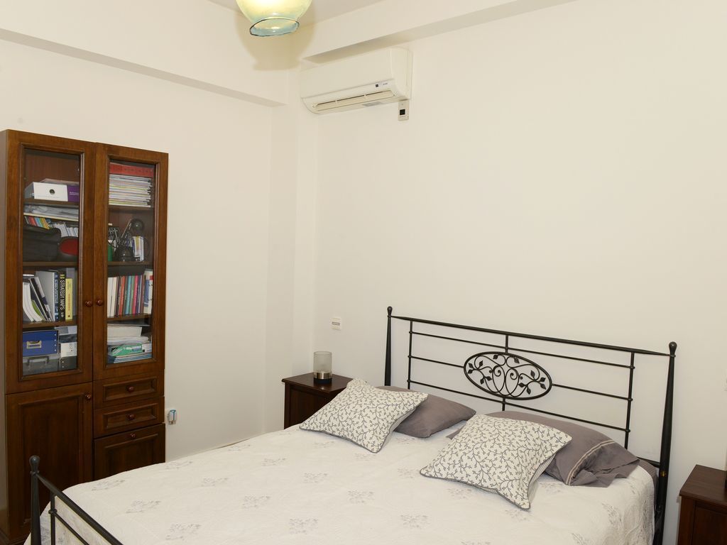 Une chambre à coucher comprenant un lit, une armoire en bois, une table de chevet et un appareil de climatisation.